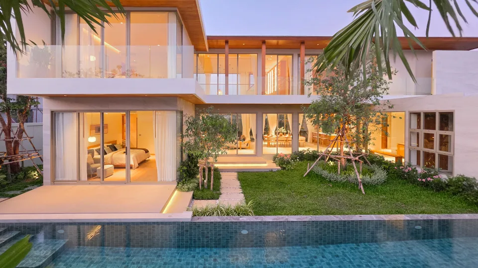Villa at dusk with the bedroom and living area lit and opening onto the lawn